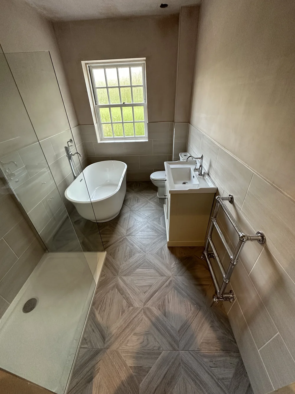 Freestanding slipper bath with chevron wood-effect floor and traditional towel radiator