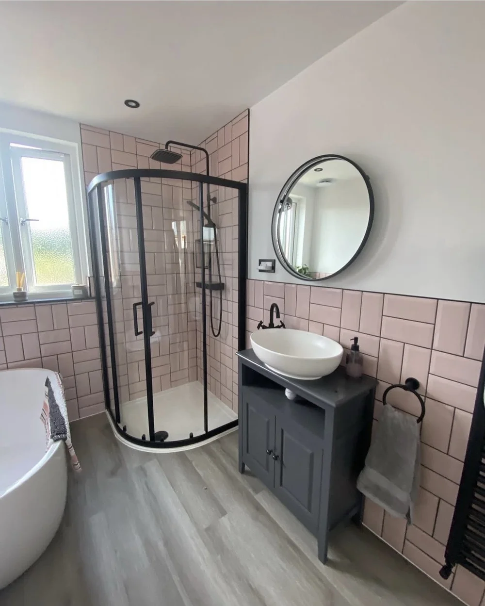 Pink metro-tile bathroom with black quadrant shower and freestanding bath