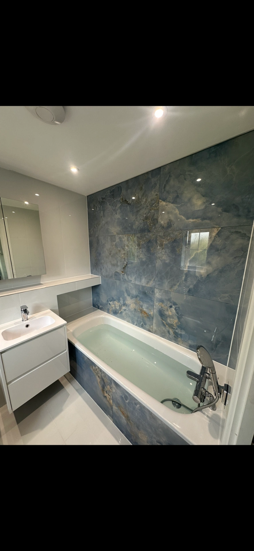 Modern bathroom with blue marble-effect feature wall and inset bath