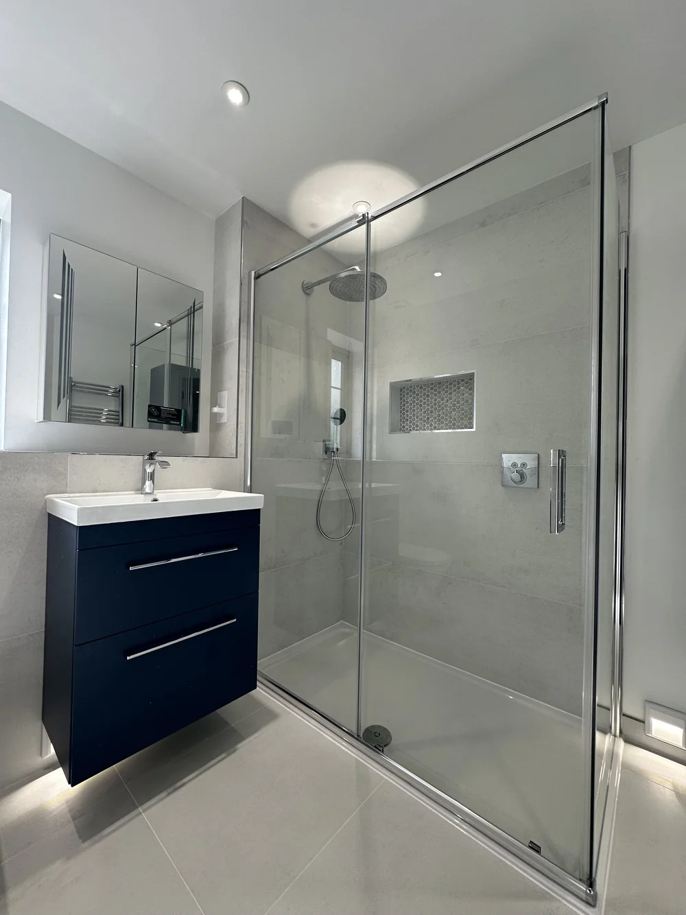 Wide walk-in shower with rainfall head, niche and navy floating vanity