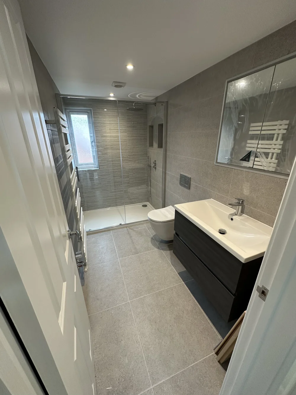 Grey walk-in shower room with dark wood vanity and chrome towel rail