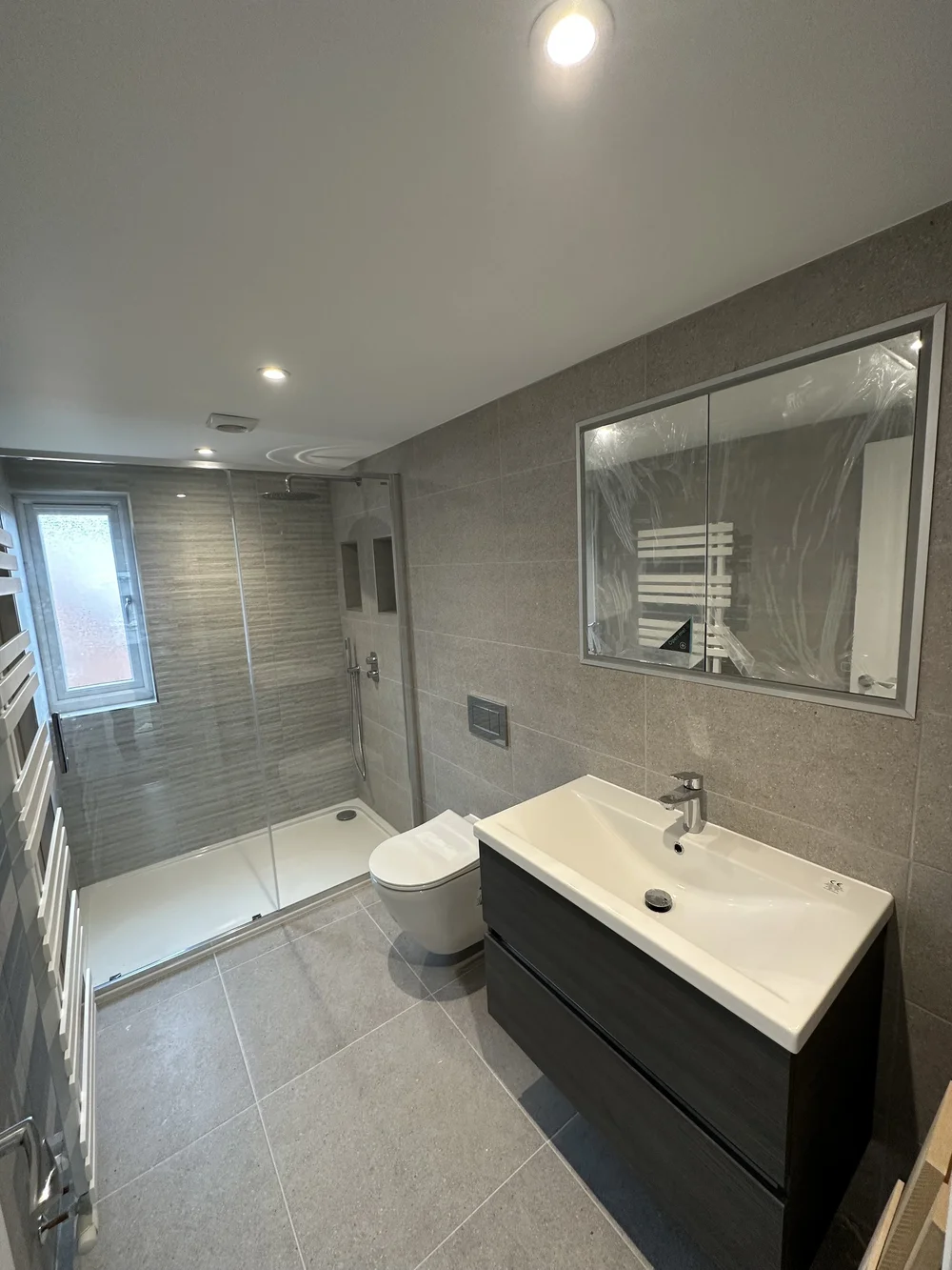 Grey-tiled shower room with large mirrored cabinet and floating vanity