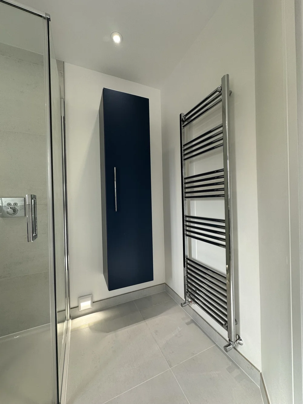Tall navy wall-hung storage cabinet beside chrome towel radiator