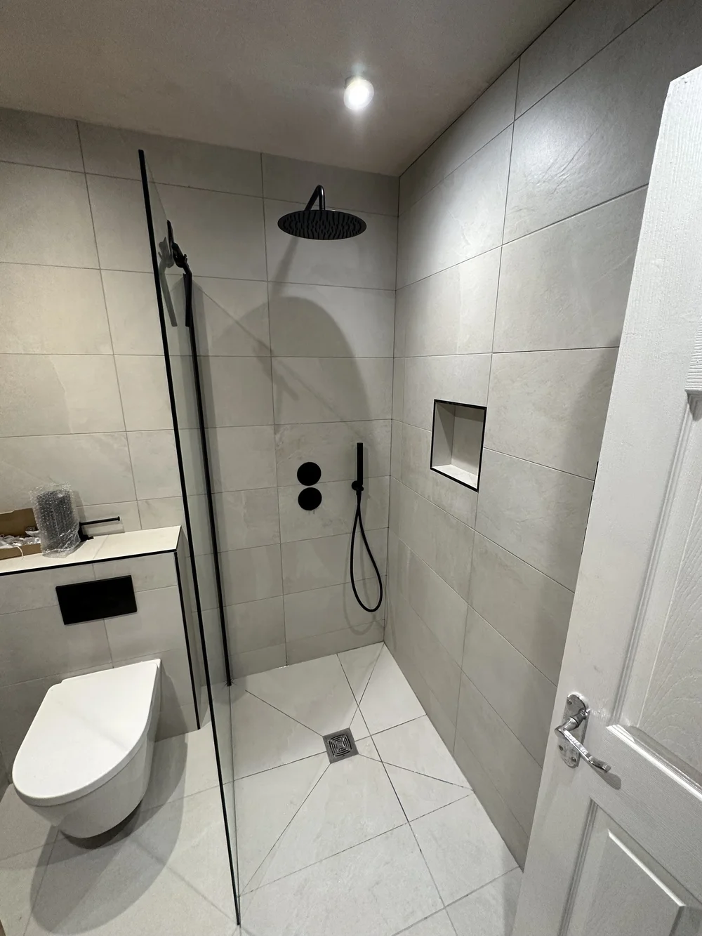 Walk-in shower with matte black rainfall head, tiled niche and wall-hung WC