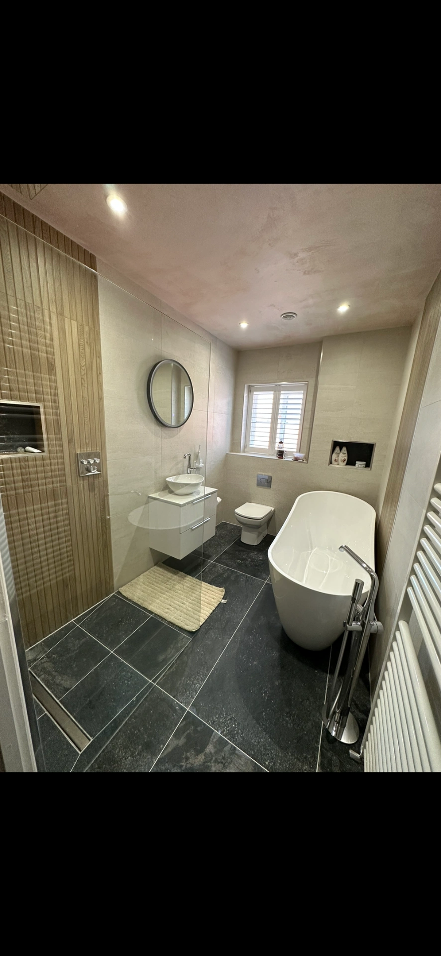Slate-tiled bathroom with freestanding bath, wall-hung vanity and round mirror